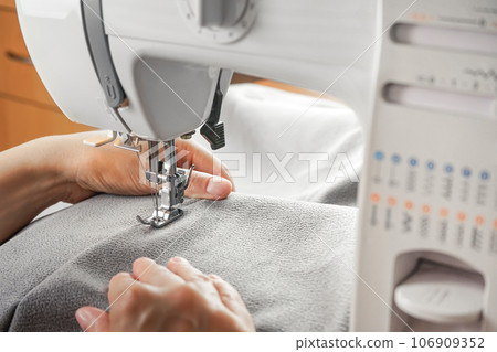 Tailor hands stitching gray fabric on modern sewing machine at workplace in atelier Tailor hands stitching gray fabric on modern sewing machine at workplace in atelier 106909352