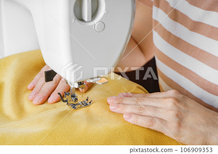 Tailor hands stitching yellow fabric on modern sewing machine at workplace in atelier Tailor hands stitching yellow fabric on modern sewing machine at workplace in atelier 106909353