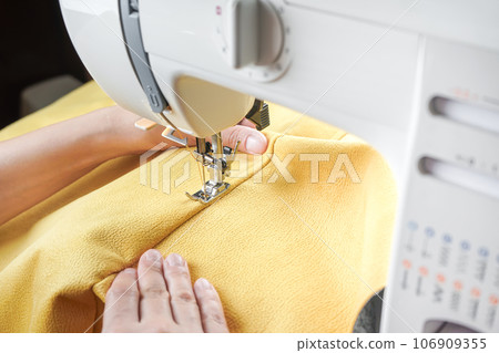 Tailor hands stitching yellow fabric on modern sewing machine at workplace in atelier Tailor hands stitching yellow fabric on modern sewing machine at workplace in atelier 106909355