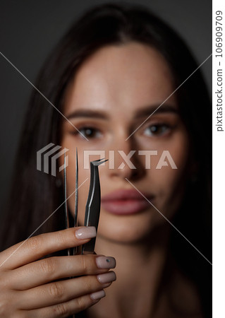 beautiful woman holding eyelashes tweezers on black background 106909709