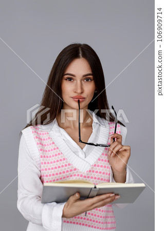 brunette woman with glasses and book on grey background 106909714