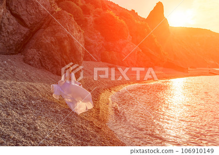 Mysterious woman silhouette long hair walks on the beach ocean water, sea nymph wind listens to the wave. Throws up a long white dress, a divine sunset. Artistic photo from the back without a face Mysterious woman silhouette long hair walks on the beach ocean water, sea nymph wind listens to the wave. Throws up a long white dress, a divine sunset. Artistic photo from the back without a face 106910149