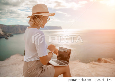 Freelance women sea working on the computer. Good looking middle aged woman typing on a laptop keyboard outdoors with a beautiful sea view. The concept of remote work. Freelance women sea working on the computer. Good looking middle aged woman typing on a laptop keyboard outdoors with a beautiful sea view. The concept of remote work. 106910160