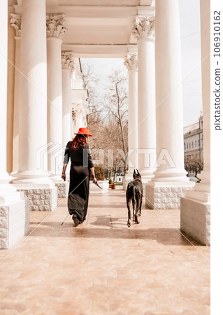A photo of a woman and her Great Dane walking through a town, taking in the sights and sounds of the urban environment. A photo of a woman and her Great Dane walking through a town, taking in the sights and sounds of the urban environment. 106910162