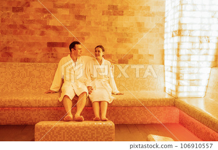 Young married couple in white bathrobes sits and relaxes in the salt room. 106910557
