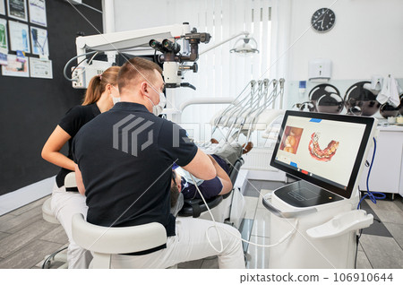 Dentist scanning patient's teeth with modern machine for intraoral scanning. Digital print of patient's teeth is on big screen. Modern high precision technologies. Concept of modern dentistry Dentist scanning patient's teeth with modern machine for intraoral scanning. Digital print of patient's teeth is on big screen. Modern high precision technologies. Concept of modern dentistry 106910644
