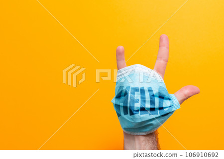 World Hello day. A male's hand with a mask on, fingers spread. The inscription on the mask Hello. Yellow background. The concept of protection from the virus 106910692