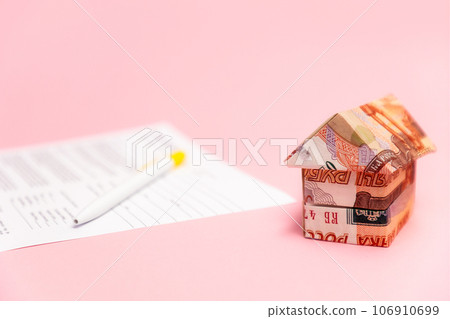 A small origami house made of Russian rubles stands next to a paper contract for the purchase of housing. Mortgage concept and leasing 106910699