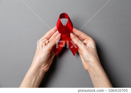 Woman's hands hold a red ribbon, a symbol of the fight against AIDS. Gray background. Copy space. Flat lay. The concept of world AIDS day 106910705