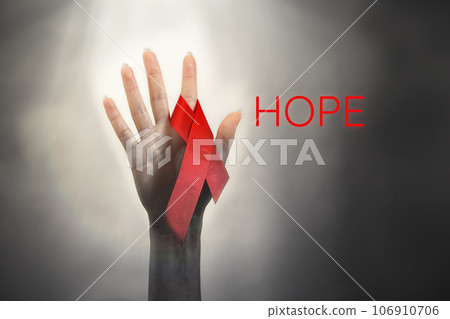 A woman's hand reaches up to light, with a red ribbon on her finger. Dark background with light at the top. The concept of the world day of fight against AIDS and the hope for a cure 106910706