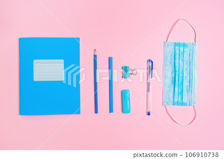 Blue copybook, protective mask and office supplies on pink background. Flat lay. Back to school banner. New normals of education Blue copybook, protective mask and office supplies on pink background. Flat lay. Back to school banner. New normals of education 106910738