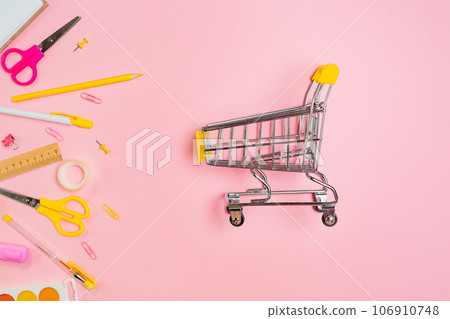 Composition of copybook, shopping and yellow office supplies on pink background. Flat lay. Concept of back to school and consumerism Composition of copybook, shopping and yellow office supplies on pink background. Flat lay. Concept of back to school and consumerism 106910748