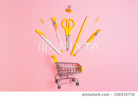 Toy shopping cart with yellow office supplies on pink background. Flat lay. Copy space. Concept of back to school and shopping Toy shopping cart with yellow office supplies on pink background. Flat lay. Copy space. Concept of back to school and shopping 106910750