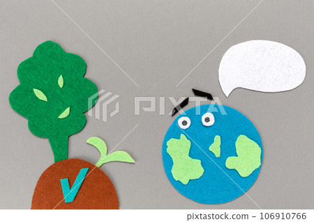 Earth Day concept. Cutted out of felt the planet Earth with emoticon and soil with a plant sprout and tree. Gray background. Flat lay. Copy space 106910766
