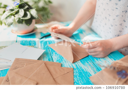 A woman reads a postcard. Hands close-up. Blue wooden table with a parcel in the background. The concept of postcrossing A woman reads a postcard. Hands close-up. Blue wooden table with a parcel in the background. The concept of postcrossing 106910780