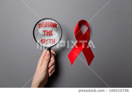 1 december - world day aids. A woman's hand holds a magnifying glass with text. Red ribbon on a gray background. Flat lay 1 december - world day aids. A woman's hand holds a magnifying glass with text. Red ribbon on a gray background. Flat lay 106910786