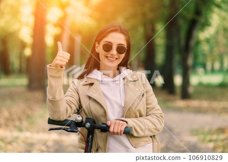 Young woman riding an electric scooter in an autumn park. Green transport, traffic jam problems. 106910829