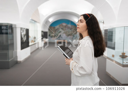 Side view of pretty young caucasian girl student visiting museum exhibition. Concept of cultural education and Museum's Day 106911026