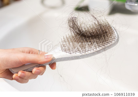 Close-up of female hand holding comb with big clump of lost hair over sink. Concept of baldness and alopecia 106911039