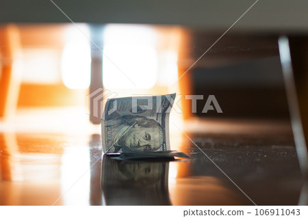 Business and finance. Close-up of lost dollar bill lying on parquet floor under furniture. Concept of devaluation and inflation Business and finance. Close-up of lost dollar bill lying on parquet floor under furniture. Concept of devaluation and inflation 106911043