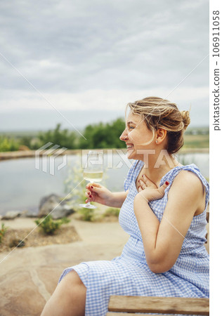 Young attractive woman in a light sundress holds a glass of champagne and laughs. 106911058
