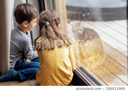 Cute children in casual clothes are sitting on the floor and playing with the cat outside Cute children in casual clothes are sitting on the floor and playing with the cat outside 106911060