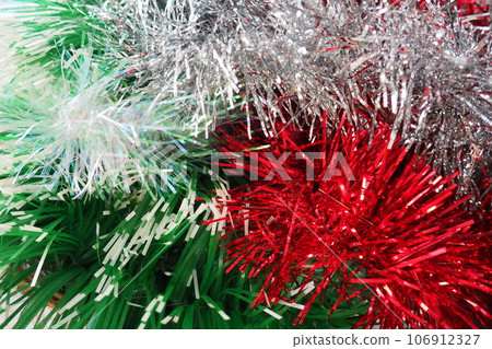 Multi-colored Christmas tinsel. Red, green, silver and white tinsel are intertwined. Festive New Year or Christmas background. Christmas decorations. Decoration of the hall for a party. Christmas boa Multi-colored Christmas tinsel. Red, green, silver and white tinsel are intertwined. Festive New Year or Christmas background. Christmas decorations. Decoration of the hall for a party. Christmas boa 106912327