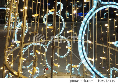 Beautiful street garlands electric lighting fixtures. New Year and Christmas decoration of city streets. Flashing sparkling white, yellow and blue light bulbs. Festive winter decoration of the city Beautiful street garlands electric lighting fixtures. New Year and Christmas decoration of city streets. Flashing sparkling white, yellow and blue light bulbs. Festive winter decoration of the city 106912349