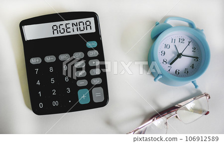 Agenda symbol. Calculator with word Agenda concept on white background with clock and glasses. 106912589