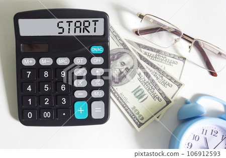 The calculator displays the text Start. Dollars, glasses and watches lie on a white background. The calculator displays the text Start. Dollars, glasses and watches lie on a white background. 106912593