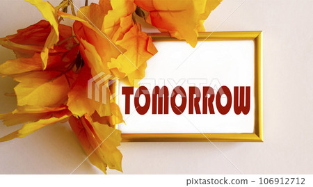 The word Tomorrow is written in a gold frame framed by yellow foliage on a light background The word Tomorrow is written in a gold frame framed by yellow foliage on a light background 106912712