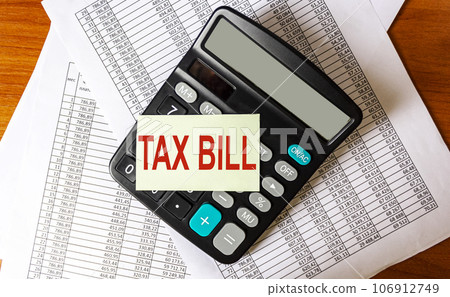 The note has the text TAX ACCOUNT, next to it are bills and a calculator on a wooden table 106912749