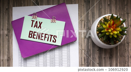 Documents are on the wooden table. notepad and sticker with text TAX BENEFITS 106912920