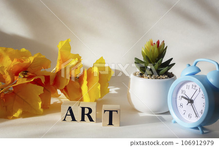 The word ART is written on a wooden block. On a white background alarm clock, cactus, yellow foliage The word ART is written on a wooden block. On a white background alarm clock, cactus, yellow foliage 106912979