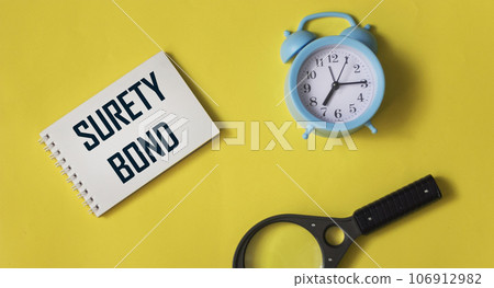 On a yellow background, an alarm clock, notepads, a notepad with the inscription SURETY BOND. On a yellow background, an alarm clock, notepads, a notepad with the inscription SURETY BOND. 106912982