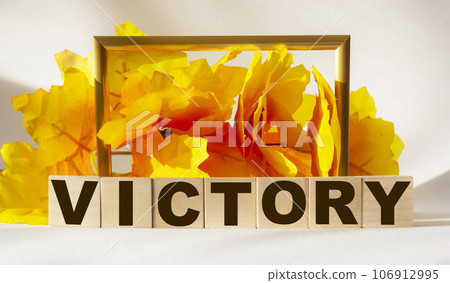 The word victory made from brown wooden letters on a light table, back with yellow foliage The word victory made from brown wooden letters on a light table, back with yellow foliage 106912995