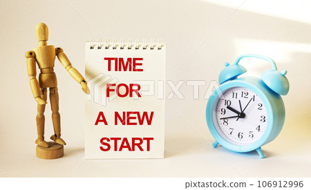 Wooden doll displays text on a white notepad TIME TO START. On white background alarm clock Wooden doll displays text on a white notepad TIME TO START. On white background alarm clock 106912996