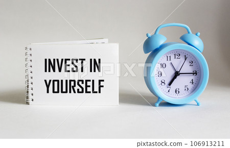 Invest in yourself, text is written on notepad and white background with alarm clock Invest in yourself, text is written on notepad and white background with alarm clock 106913211