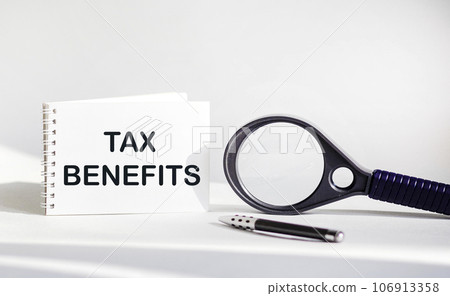 On a white background lies a magnifying glass and a notepad with the inscription - TAX BENEFITS 106913358