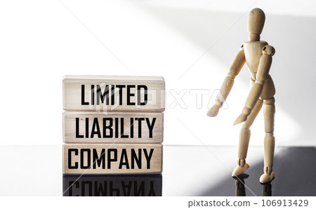 Text Limited Liability Company on a wooden block with a wooden doll on a light background . 106913429