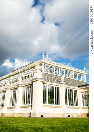 A historic white stone and large glass house under the blue sky in Kew Gardens on the outskirts of London 106913474