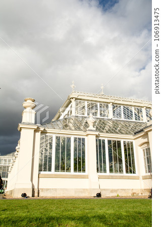 A historic white stone and large glass house under the blue sky in Kew Gardens on the outskirts of London A historic white stone and large glass house under the blue sky in Kew Gardens on the outskirts of London 106913475