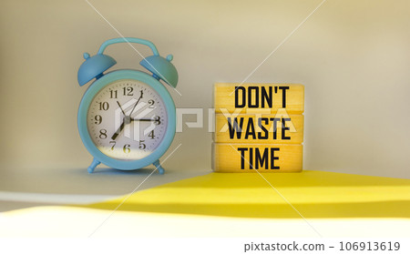 Don't waste time written on wooden blocks on a light background, next to an alarm clock. Don't waste time written on wooden blocks on a light background, next to an alarm clock. 106913619