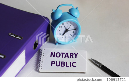NOTARY PUBLIC written on a notebook next to a clock, a pen and a purple folder on a white background 106913721