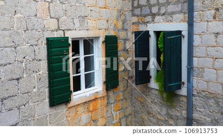The old window with green closed shutters on an old house. Vintage texture. Herceg Novi, Montenegro, old stone house. Architecture of the Adriatic region. Fixing windows and shutters to the wall 106913753