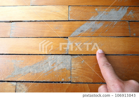 Old, scratched parquet flooring needs maintenance. the parquet is damaged by scratches from prolonged use. Master's hands show damage to the floor. 106913843
