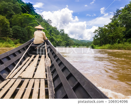 Helmsman with traditional cone hat sails on Pai river with long tail boat, Thailand Helmsman with traditional cone hat sails on Pai river with long tail boat, Thailand 106914096