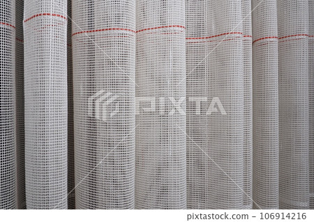 White coarse cotton or linen curtains made of weaves of thin threads. Simple compact economical apartment interior. Window decoration in the room. Red stripe 106914216