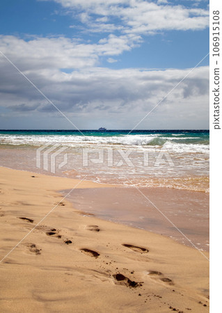 Footprints in the sand of Jandia Beach in front of the sea and a cruise ship, Fuerteventura, Canary Islands, Spain 106915108