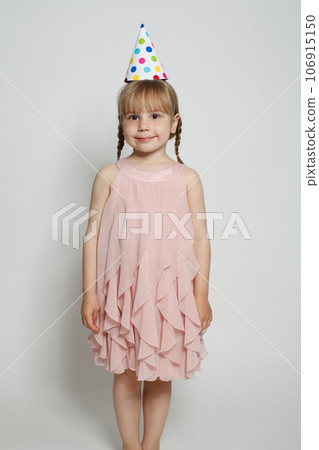 Pretty child girl wearing pink dress and birthday party hat standing on white background 106915150